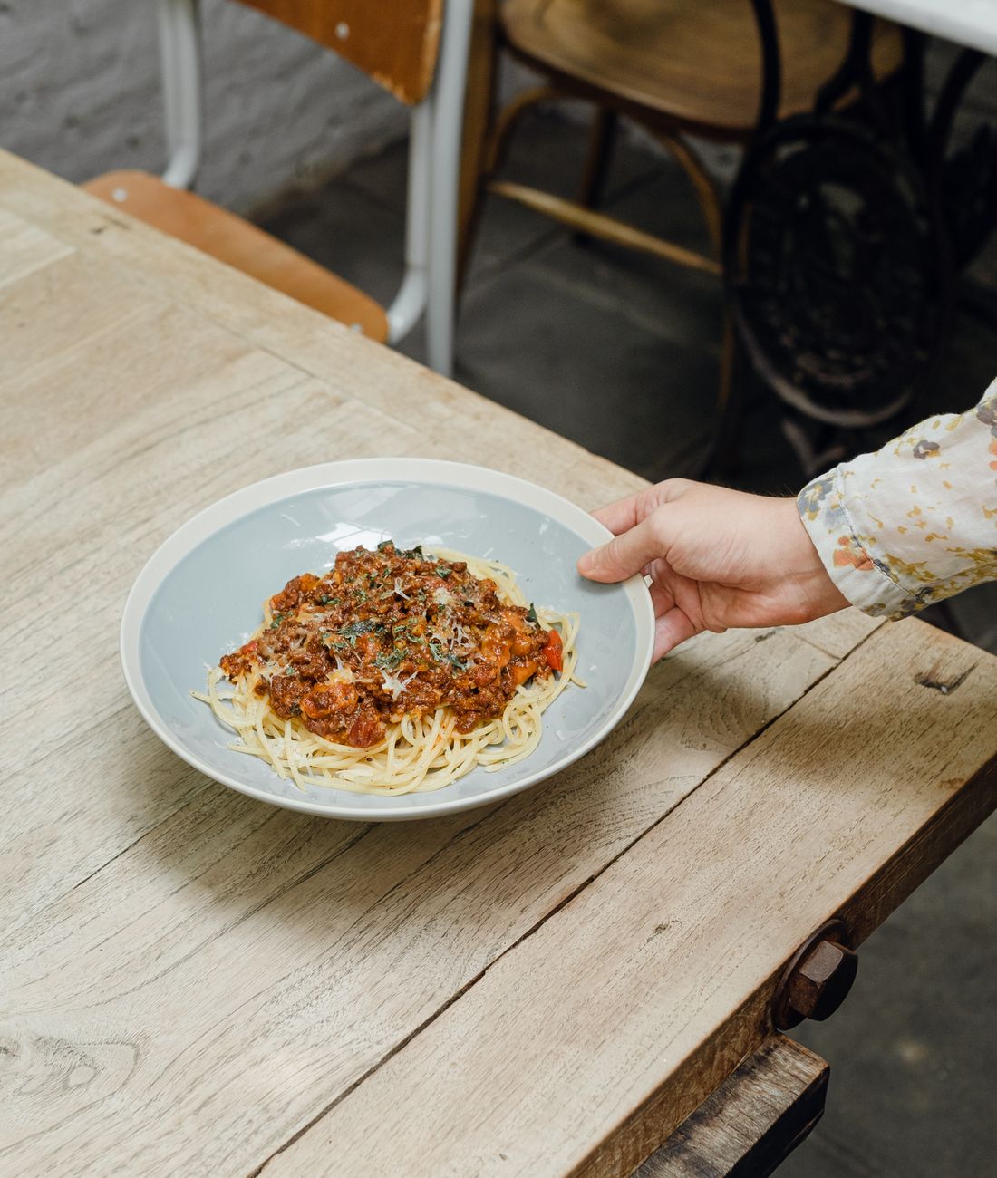 A plate of spaghetti bolognese being set down on a table